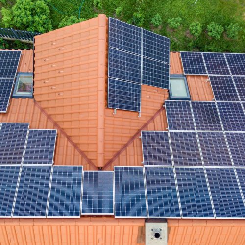 Aerial top view of new modern residential house cottage with blue shiny solar photo voltaic panels system on roof. Renewable ecological green energy production concept.